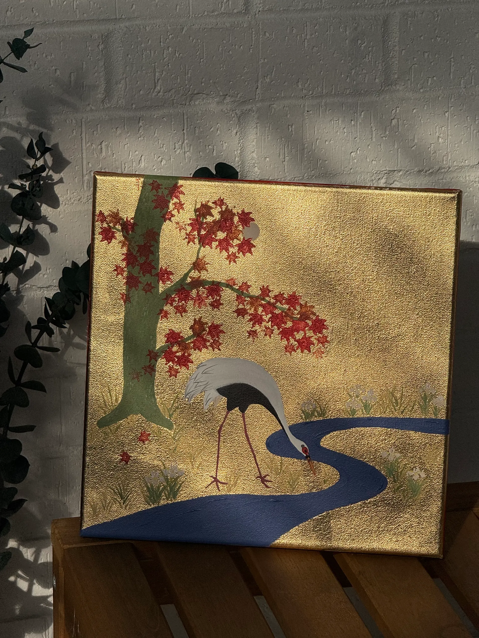 A white crane by a blue stream beneath a red maple tree on a gold ground.