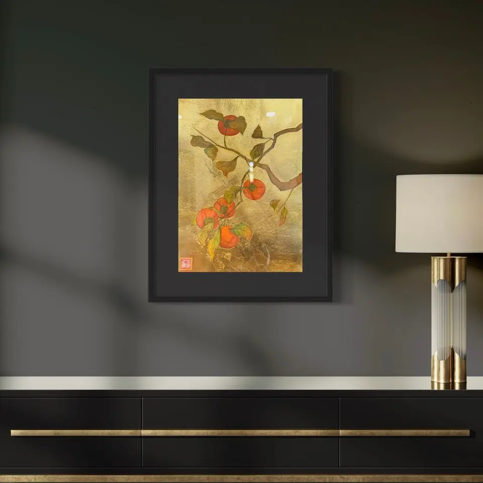 A framed painting of orange persimmons and green leaves with gold accents.